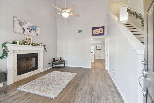 living room featuring hardwood / wood-style floors, a stone fireplace, ceiling fan, and a towering ceiling