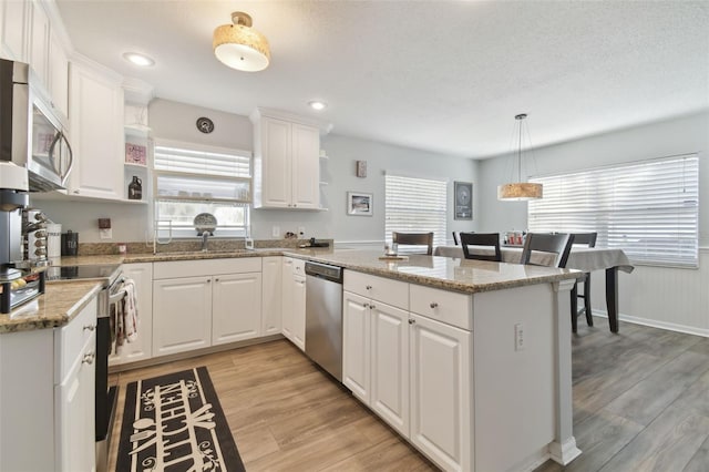 kitchen featuring white cabinetry, light stone counters, hanging light fixtures, kitchen peninsula, and stainless steel appliances