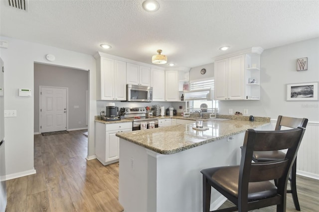 kitchen with white cabinetry, stainless steel appliances, kitchen peninsula, and light stone countertops