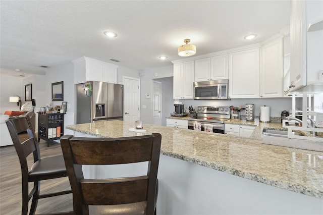 kitchen with light stone counters, kitchen peninsula, stainless steel appliances, light hardwood / wood-style floors, and white cabinets