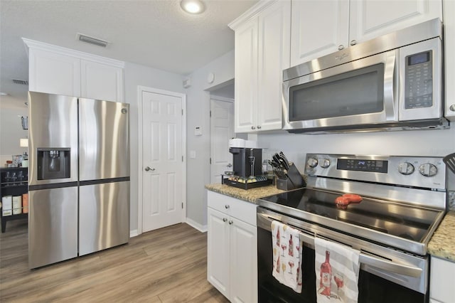 kitchen featuring light hardwood / wood-style flooring, light stone countertops, white cabinets, and appliances with stainless steel finishes