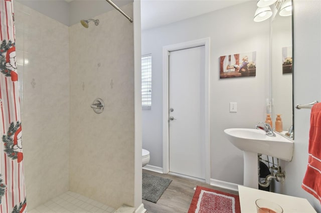 bathroom with wood-type flooring, toilet, and tiled shower