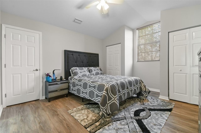 bedroom with wood-type flooring, lofted ceiling, two closets, and ceiling fan