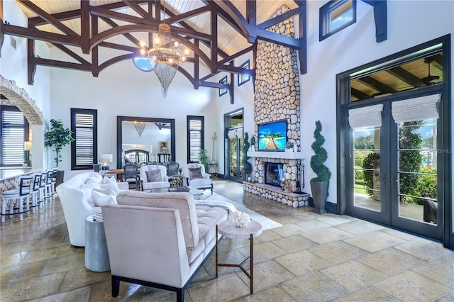 living room with a stone fireplace, high vaulted ceiling, beamed ceiling, an inviting chandelier, and french doors