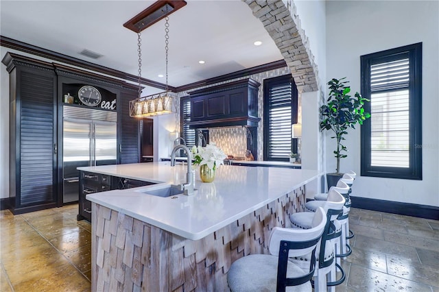 kitchen with stainless steel built in refrigerator, sink, a kitchen breakfast bar, hanging light fixtures, and a kitchen island with sink