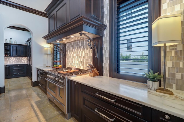 kitchen with custom exhaust hood, range with two ovens, ornamental molding, light stone countertops, and decorative backsplash