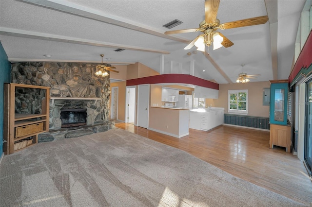 unfurnished living room with ceiling fan, vaulted ceiling with beams, a fireplace, light hardwood / wood-style floors, and a textured ceiling