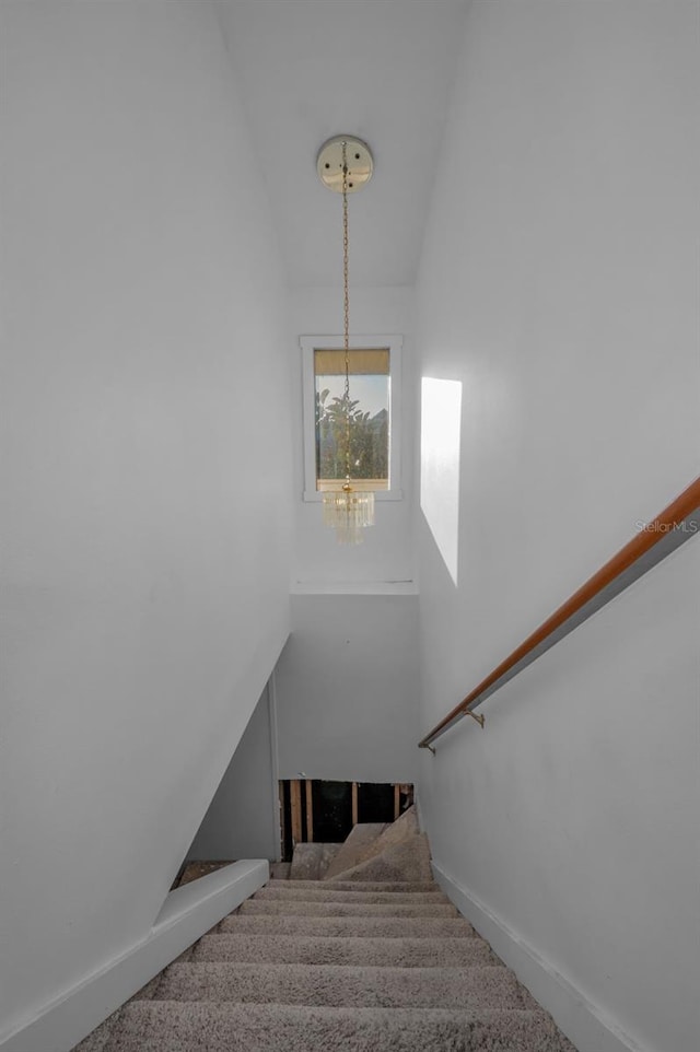 stairway featuring vaulted ceiling, carpet, and a notable chandelier