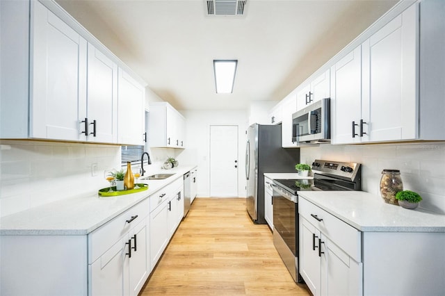 kitchen featuring appliances with stainless steel finishes, sink, white cabinets, and light wood-type flooring