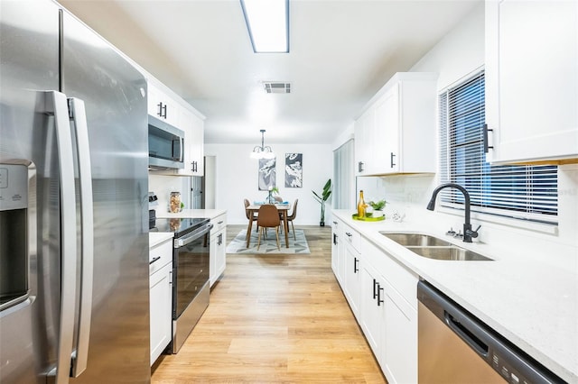 kitchen featuring decorative light fixtures, sink, white cabinets, light hardwood / wood-style floors, and stainless steel appliances