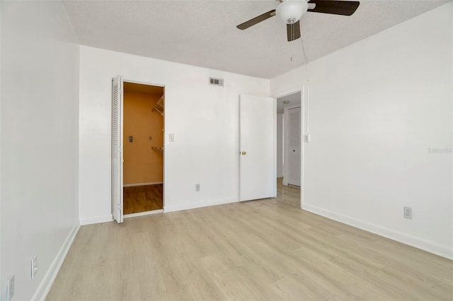 unfurnished bedroom with ceiling fan, a walk in closet, a textured ceiling, and light wood-type flooring