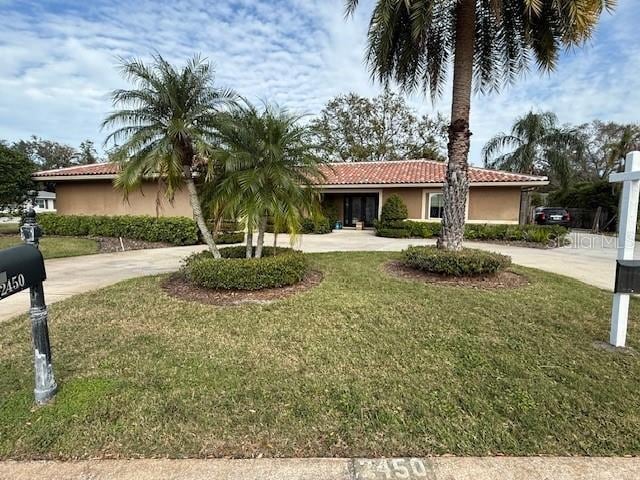 ranch-style house with a tiled roof, a front yard, curved driveway, and stucco siding