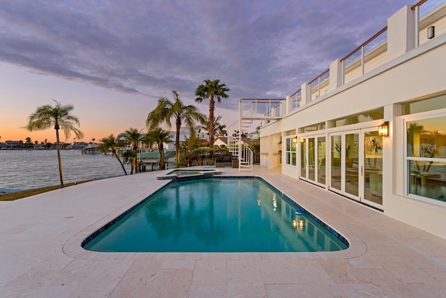 pool at dusk featuring a water view, an in ground hot tub, and a patio