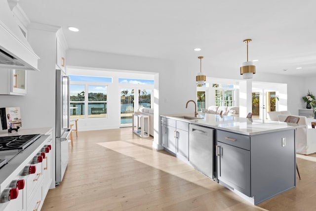 kitchen with sink, custom exhaust hood, hanging light fixtures, a center island with sink, and stainless steel appliances