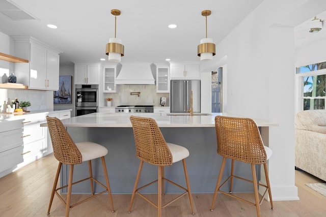 kitchen with custom exhaust hood, a breakfast bar area, white cabinets, and appliances with stainless steel finishes