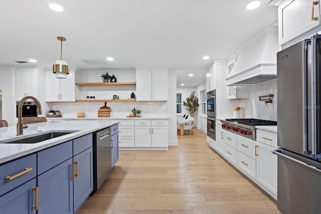 kitchen featuring premium range hood, appliances with stainless steel finishes, white cabinetry, sink, and blue cabinetry