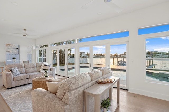 living room featuring light wood-type flooring, ceiling fan, and a water view