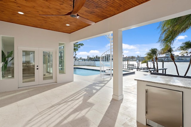 view of pool with exterior bar, a patio area, french doors, and a water view