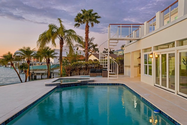 pool at dusk featuring an in ground hot tub, a water view, a patio, and a boat dock