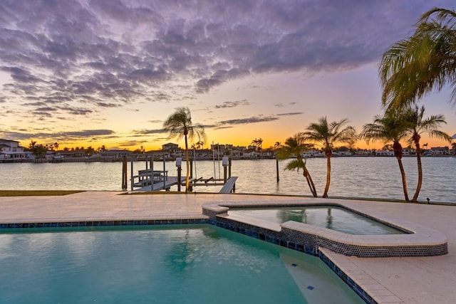 pool at dusk with an in ground hot tub and a water view