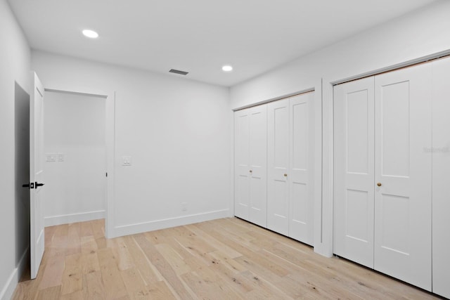 unfurnished bedroom featuring multiple closets and light hardwood / wood-style floors