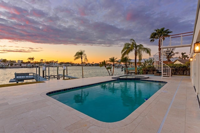 pool at dusk featuring a patio, a water view, a boat dock, and an in ground hot tub