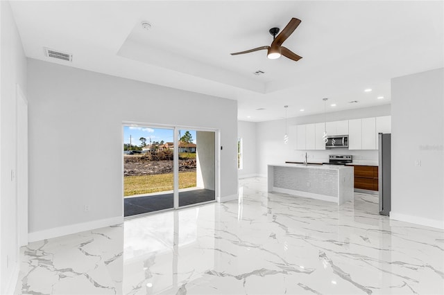 kitchen featuring white cabinetry, appliances with stainless steel finishes, a tray ceiling, and an island with sink