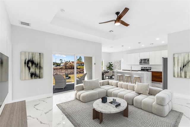 living room with a raised ceiling, sink, and ceiling fan