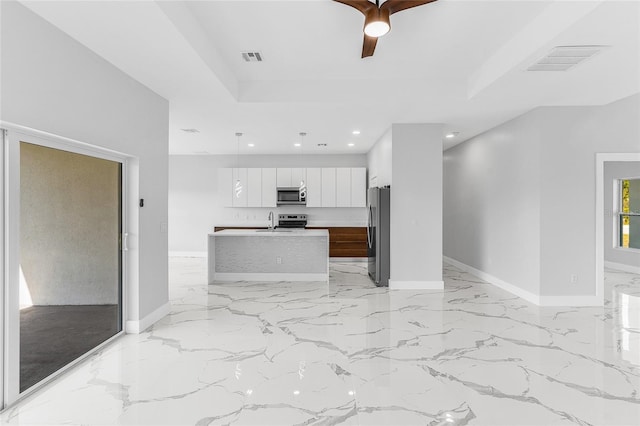 interior space with a raised ceiling, white cabinetry, appliances with stainless steel finishes, and a center island with sink