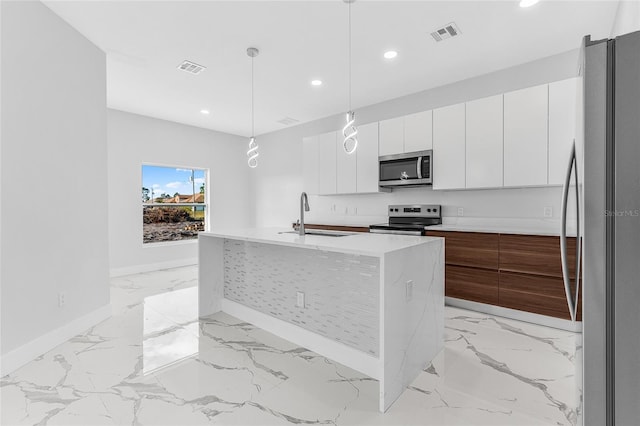 kitchen with sink, appliances with stainless steel finishes, an island with sink, pendant lighting, and white cabinets