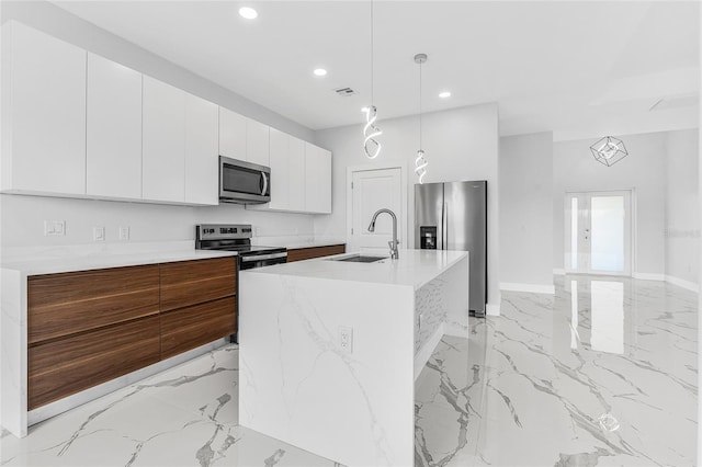 kitchen with sink, white cabinetry, decorative light fixtures, appliances with stainless steel finishes, and a kitchen island with sink