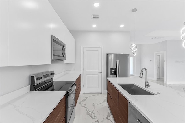 kitchen with sink, appliances with stainless steel finishes, light stone counters, white cabinets, and decorative light fixtures