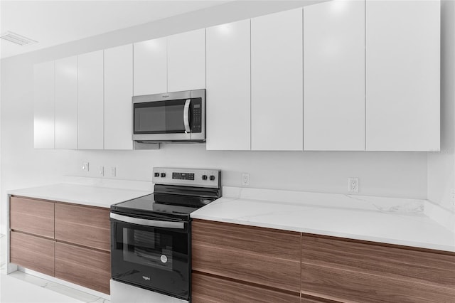 kitchen with white cabinetry, appliances with stainless steel finishes, and light stone counters