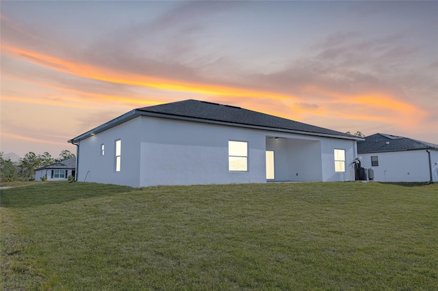 back house at dusk featuring a lawn