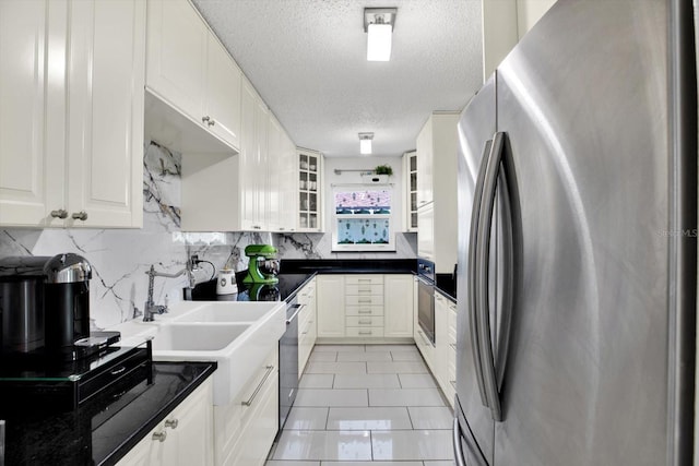 kitchen with sink, a textured ceiling, light tile patterned floors, stainless steel refrigerator, and white cabinets