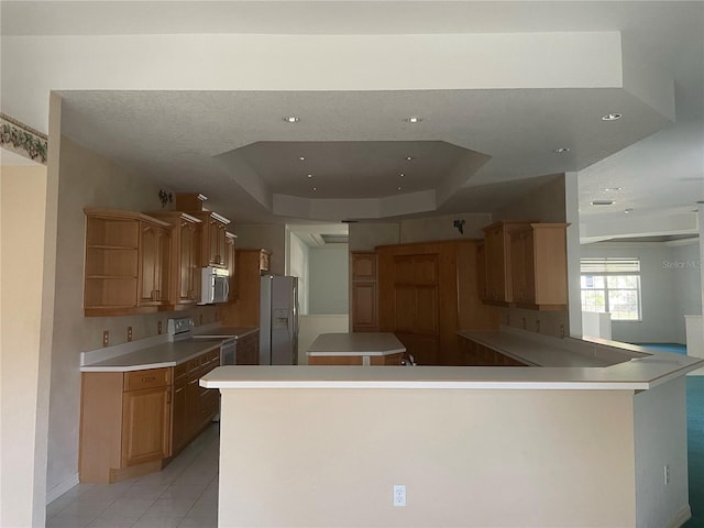 kitchen with a tray ceiling, white appliances, kitchen peninsula, and light tile patterned flooring