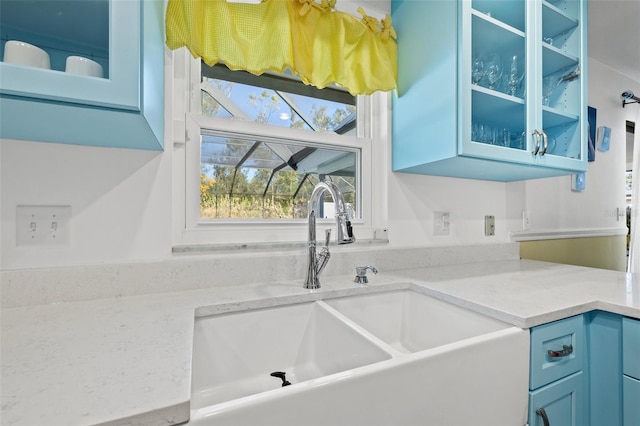 kitchen featuring light stone counters, sink, and blue cabinetry