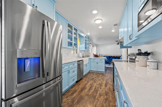 kitchen featuring sink, dark wood-type flooring, stainless steel appliances, light stone countertops, and blue cabinetry