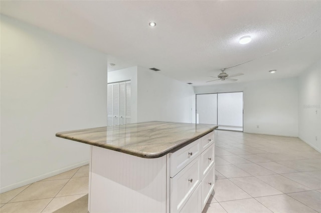 kitchen with light tile patterned floors, ceiling fan, white cabinetry, a textured ceiling, and a kitchen island