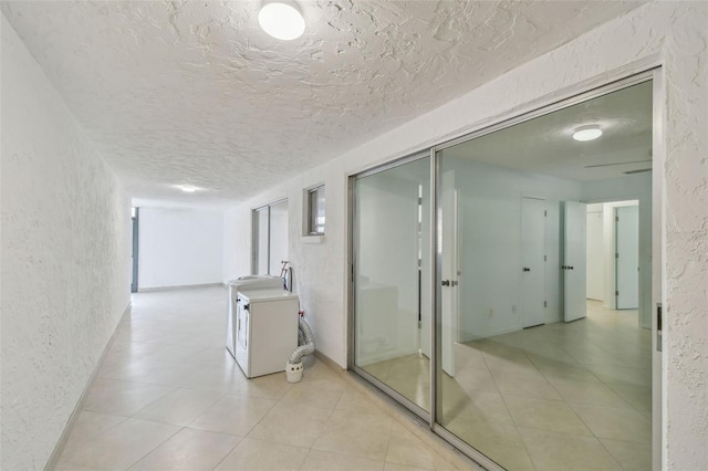 hallway featuring light tile patterned floors, washing machine and dryer, and a textured ceiling