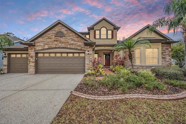 traditional-style house featuring a garage, driveway, stone siding, and stucco siding