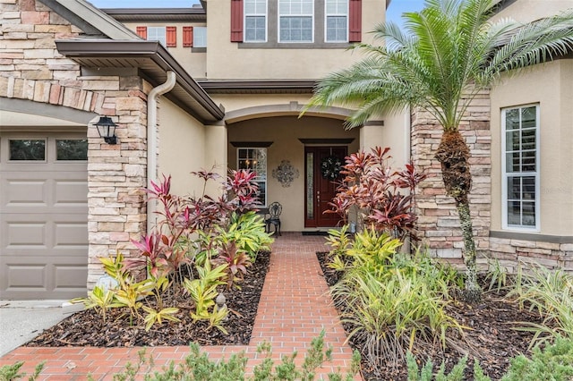 entrance to property featuring stone siding, an attached garage, and stucco siding