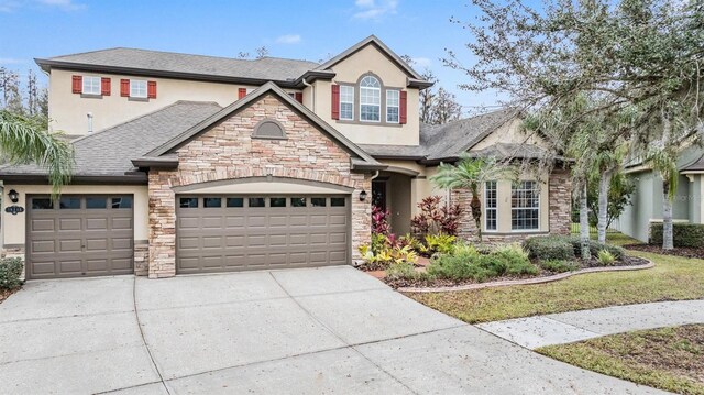 view of front facade featuring an attached garage, stone siding, driveway, and stucco siding