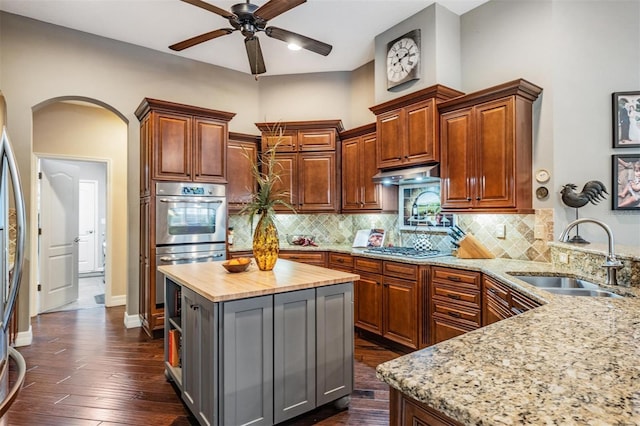 kitchen with arched walkways, wood counters, appliances with stainless steel finishes, under cabinet range hood, and a sink