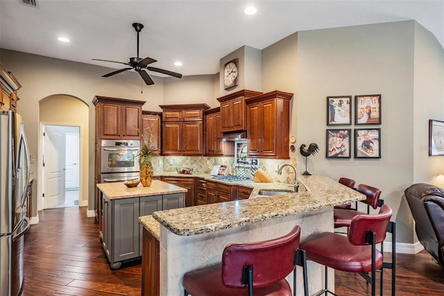 kitchen with arched walkways, decorative backsplash, appliances with stainless steel finishes, a peninsula, and a sink