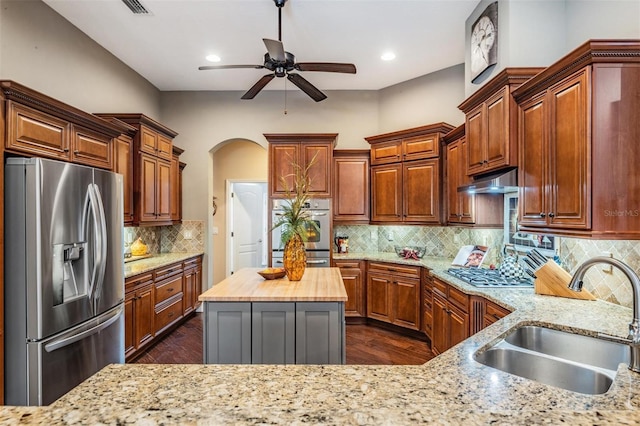 kitchen featuring arched walkways, butcher block counters, decorative backsplash, appliances with stainless steel finishes, and a sink