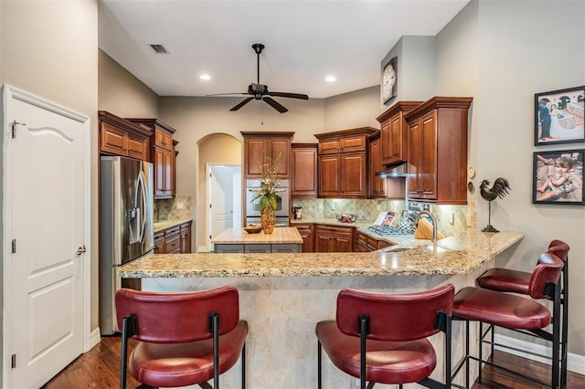 kitchen featuring under cabinet range hood, a peninsula, a sink, visible vents, and stainless steel refrigerator with ice dispenser