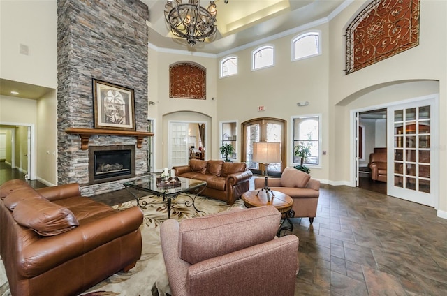 living room with ornamental molding, a stone fireplace, a chandelier, and french doors