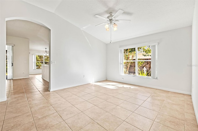 spare room with ceiling fan, arched walkways, light tile patterned flooring, baseboards, and vaulted ceiling