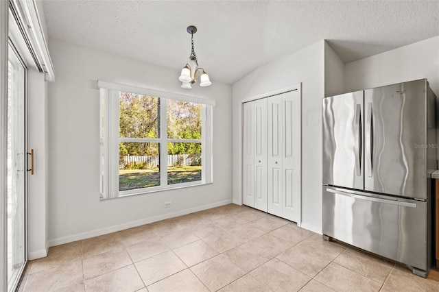 unfurnished dining area with light tile patterned flooring, a textured ceiling, and a notable chandelier